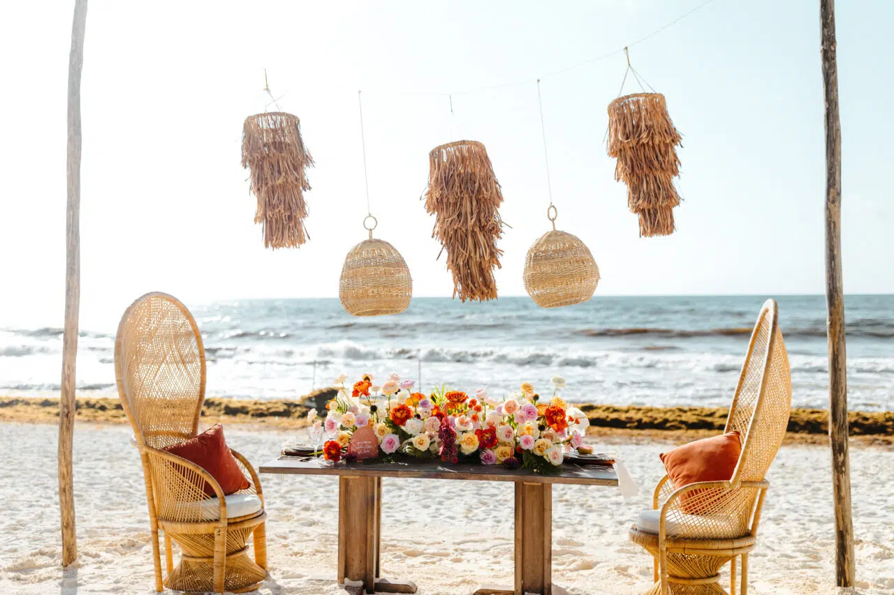 Mesa de novios con sillas de ratán y flores sobre la arena