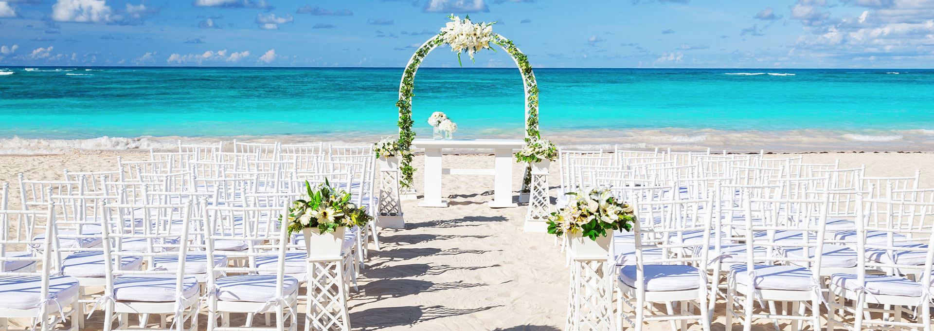 Ceremonia de boda blanca en la playa con arco floral frente al Caribe turquesa